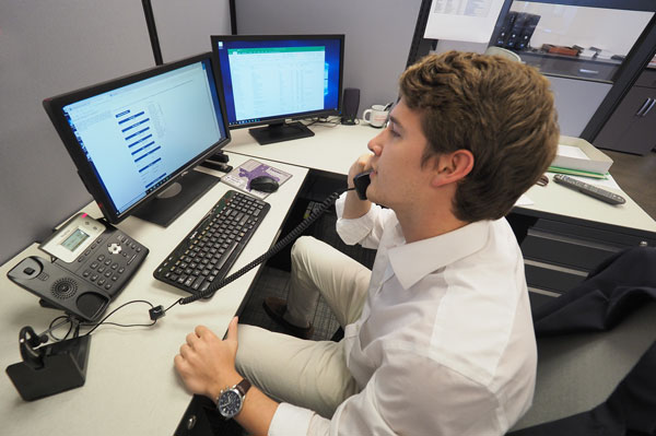 young intern guy in white collar shirt on phone looking at computer screen with two screens in office scenario above angle peregrine energy partners contact us today